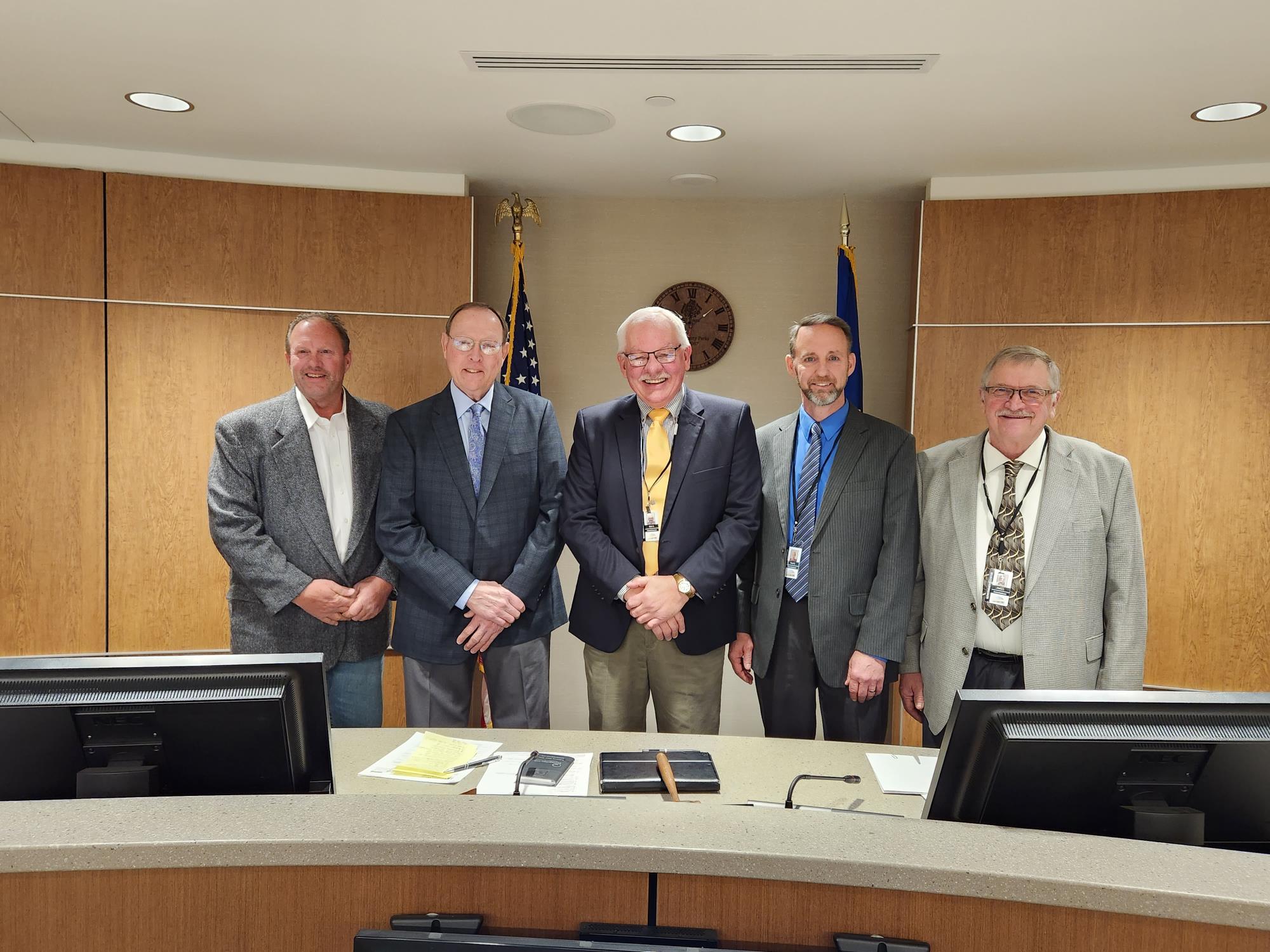 All Commissioners in the board room standing infront of the United States and Minnesota flag. 